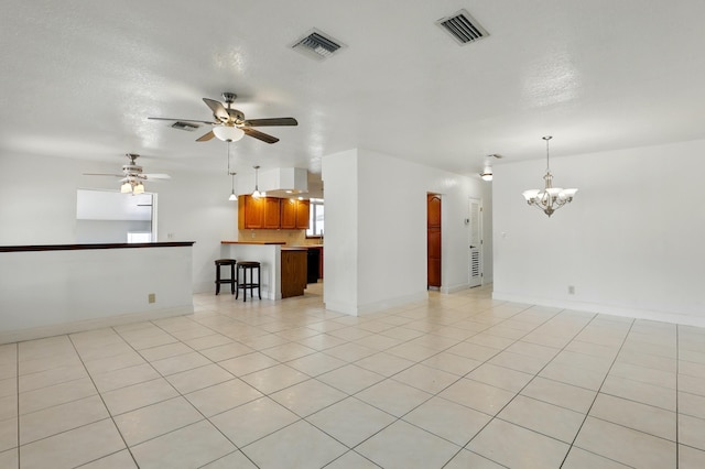 unfurnished living room featuring ceiling fan with notable chandelier, baseboards, visible vents, and light tile patterned floors