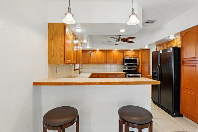 kitchen featuring tasteful backsplash, tile counters, stainless steel appliances, a peninsula, and visible vents
