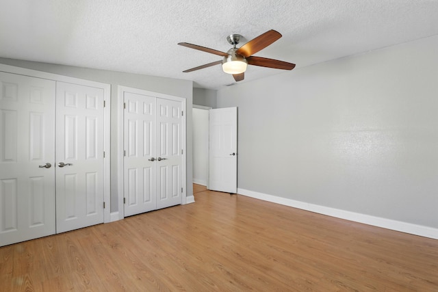 unfurnished bedroom with two closets, ceiling fan, a textured ceiling, light wood finished floors, and baseboards