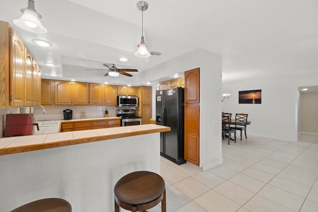 kitchen with pendant lighting, tile counters, kitchen peninsula, stainless steel appliances, and ceiling fan