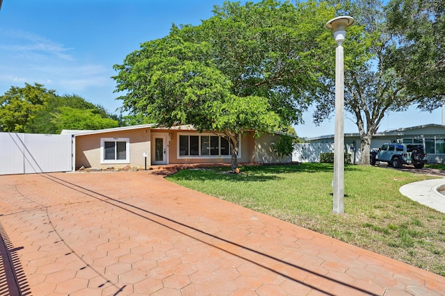 view of front facade with stucco siding, a front yard, fence, a gate, and concrete driveway
