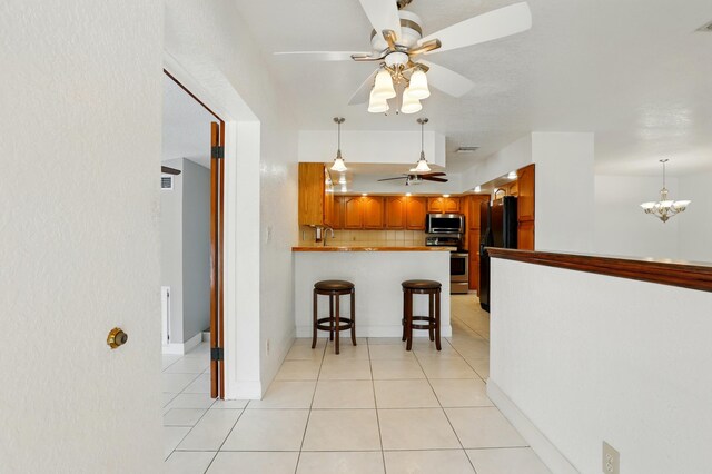 kitchen featuring a peninsula, light tile patterned flooring, backsplash, ceiling fan with notable chandelier, and appliances with stainless steel finishes