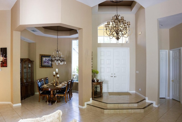 tiled foyer entrance with a raised ceiling, a towering ceiling, and a notable chandelier