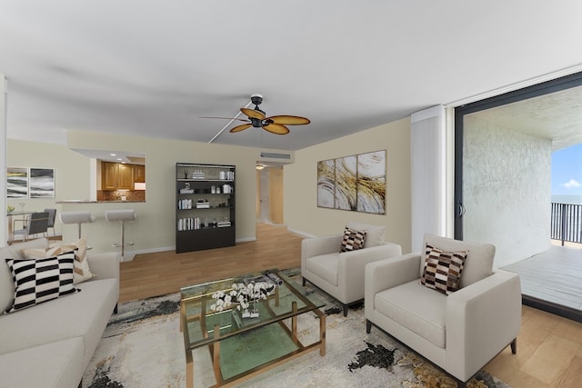 living room featuring light wood-style flooring, visible vents, baseboards, and a ceiling fan