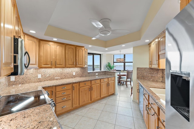 kitchen featuring light stone countertops, appliances with stainless steel finishes, decorative backsplash, and a tray ceiling