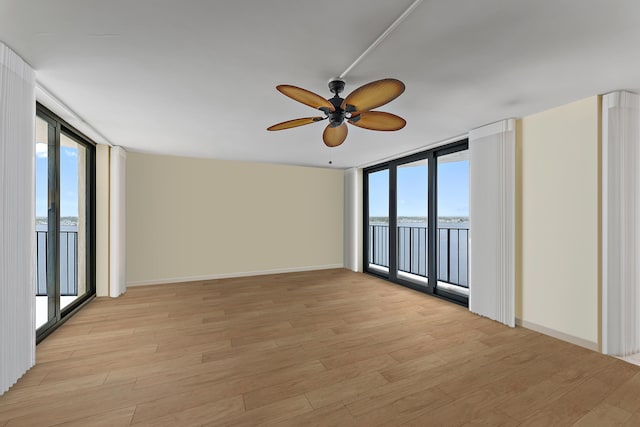 spare room with baseboards, a wall of windows, and light wood-style floors