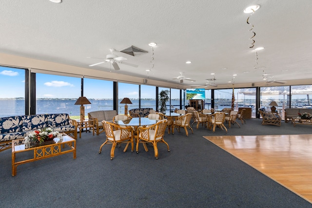 carpeted dining area featuring a water view, ceiling fan, and a textured ceiling