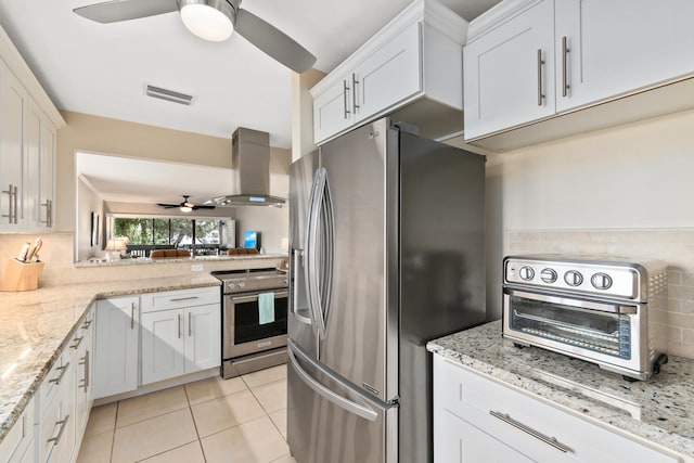 kitchen featuring appliances with stainless steel finishes, white cabinets, backsplash, ceiling fan, and wall chimney range hood