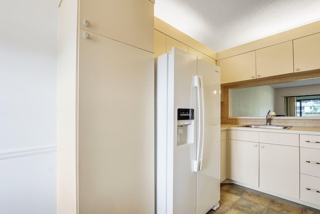 kitchen featuring a textured ceiling, backsplash, white fridge with ice dispenser, and sink