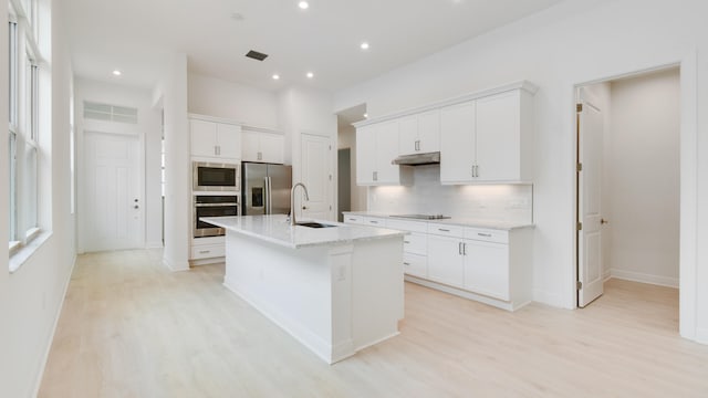 kitchen with white cabinetry, stainless steel appliances, a center island with sink, and sink