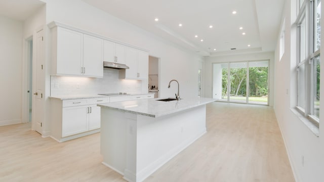 kitchen with white cabinets, a center island with sink, black electric cooktop, light hardwood / wood-style floors, and sink