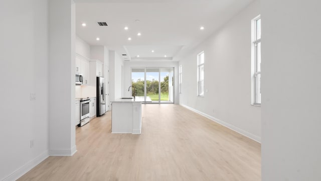 kitchen with white cabinets, light hardwood / wood-style floors, sink, and an island with sink