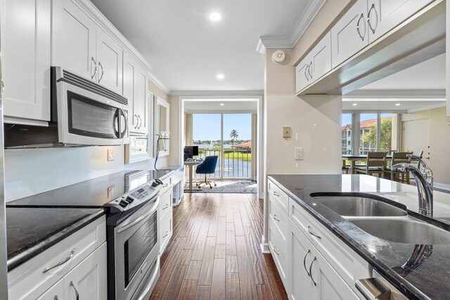 kitchen featuring white cabinets, stainless steel appliances, crown molding, and dark wood-type flooring