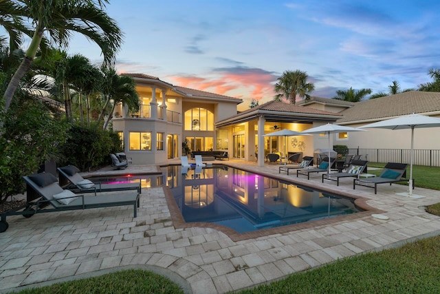 pool at dusk with area for grilling, an outdoor hangout area, an outdoor bar, and a patio