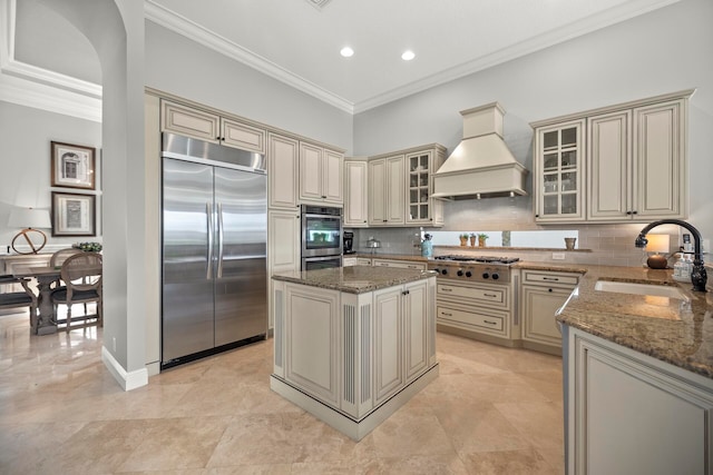 kitchen featuring appliances with stainless steel finishes, a kitchen island, custom exhaust hood, cream cabinets, and sink