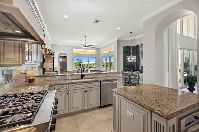 kitchen featuring an island with sink, sink, backsplash, stainless steel appliances, and ceiling fan with notable chandelier