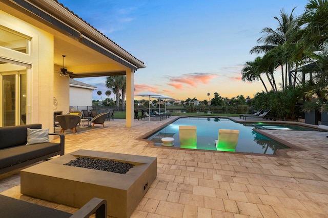 pool at dusk featuring a patio, an outdoor living space with a fire pit, and ceiling fan