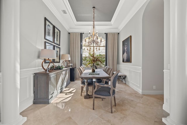 dining space featuring a notable chandelier, a raised ceiling, ornamental molding, and ornate columns