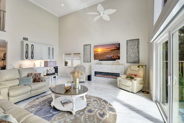 living room featuring ceiling fan, ornamental molding, a fireplace, and a high ceiling