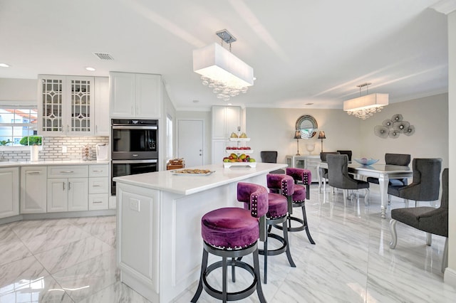 kitchen with a center island, a breakfast bar area, white cabinets, decorative light fixtures, and double oven