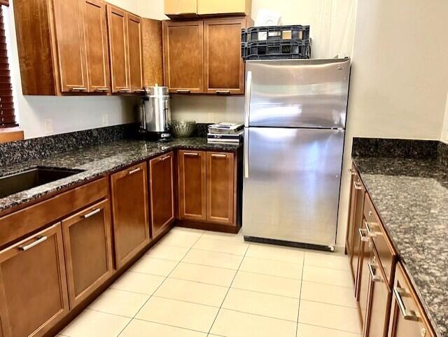 kitchen featuring dark stone counters, sink, light tile patterned floors, and stainless steel fridge