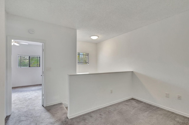 empty room featuring a textured ceiling, ceiling fan, and light carpet