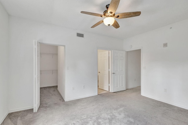 unfurnished bedroom with a closet, light colored carpet, ceiling fan, and a walk in closet