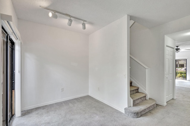 empty room with ceiling fan, light colored carpet, a textured ceiling, and track lighting