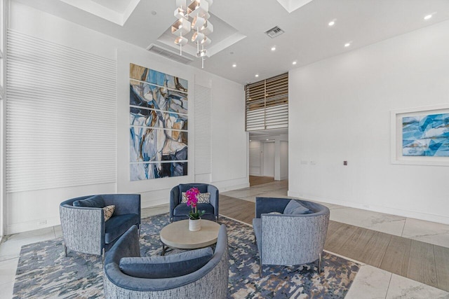 living area with an inviting chandelier, light wood-type flooring, and a raised ceiling