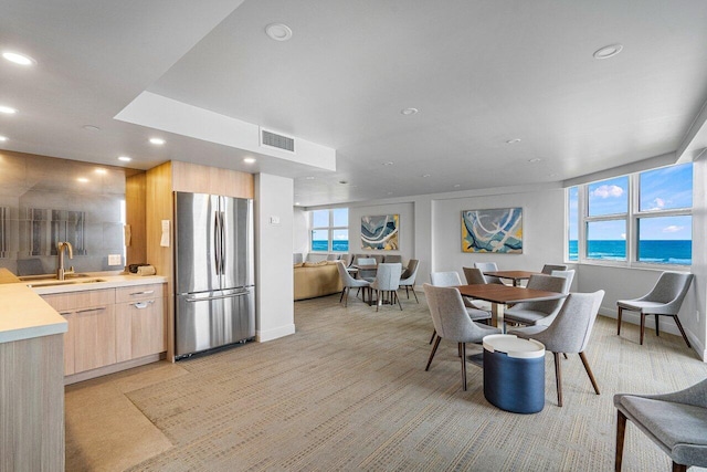 dining space featuring a water view, light colored carpet, plenty of natural light, and sink