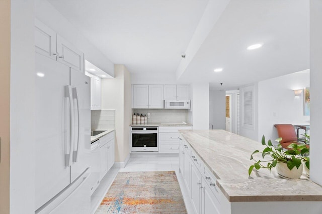 kitchen featuring backsplash, white appliances, white cabinetry, and light stone counters