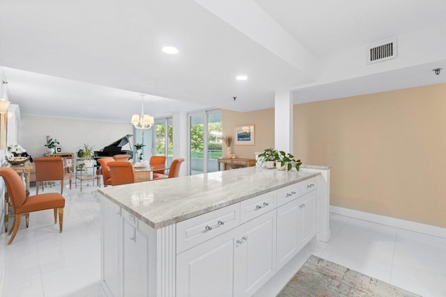 kitchen with light tile patterned flooring, white cabinetry, hanging light fixtures, a kitchen island, and light stone countertops