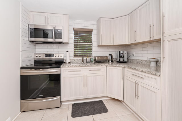 kitchen featuring light stone counters, white cabinetry, backsplash, appliances with stainless steel finishes, and light tile patterned floors