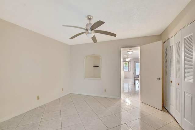 unfurnished bedroom with a closet, ceiling fan, light tile patterned floors, and a textured ceiling