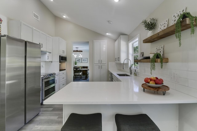 kitchen featuring a kitchen breakfast bar, kitchen peninsula, white cabinets, and appliances with stainless steel finishes