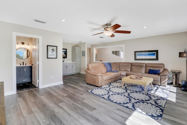 living room featuring ceiling fan, sink, and light wood-type flooring