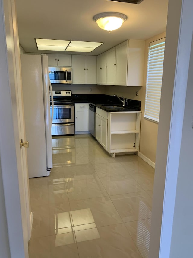 2936 Lake Shore Dr Unit 101, Riviera Beach, FL 33404 - kitchen featuring stainless steel appliances, a sink, white cabinetry, dark countertops, and baseboards