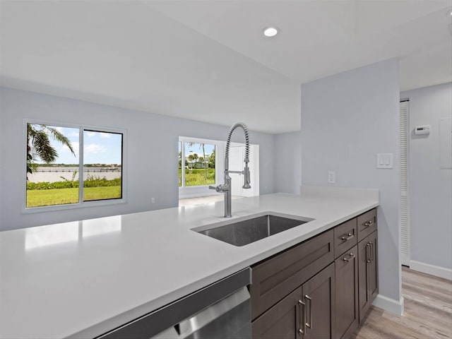 kitchen featuring light wood-type flooring, dark brown cabinets, kitchen peninsula, and sink