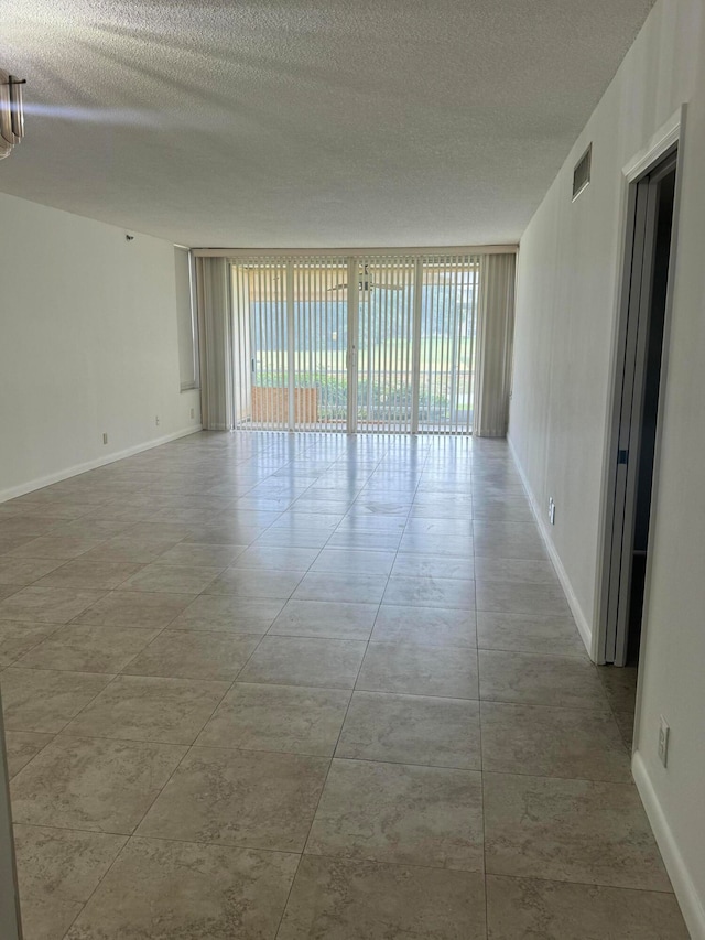 spare room with a textured ceiling, a wall of windows, and light tile patterned floors