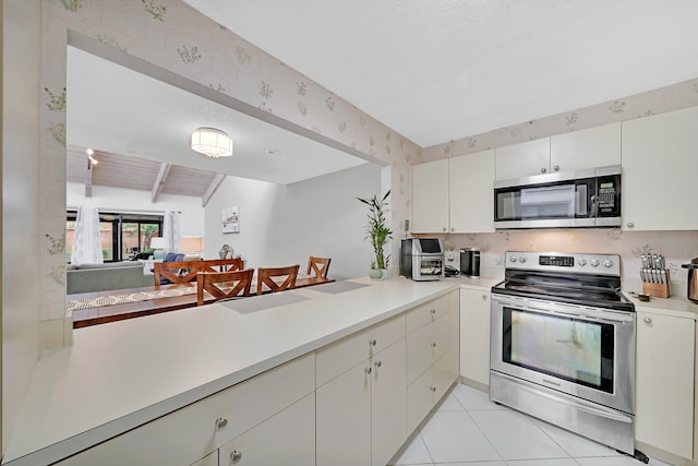 kitchen with vaulted ceiling with beams, light tile patterned floors, kitchen peninsula, white cabinetry, and stainless steel appliances