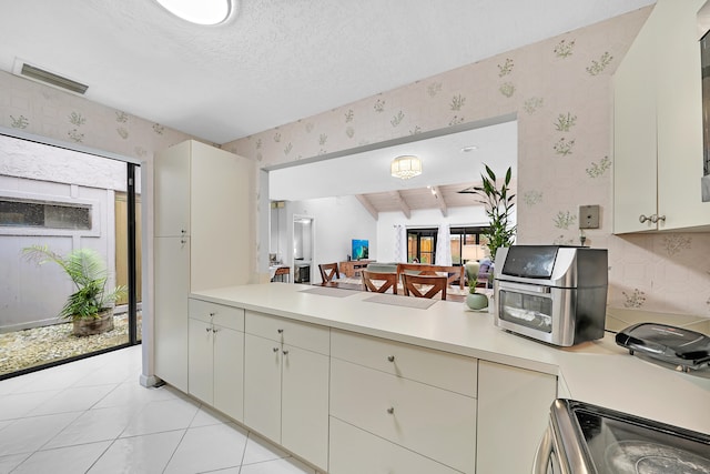 kitchen with a textured ceiling, stainless steel range oven, vaulted ceiling with beams, and light tile patterned floors