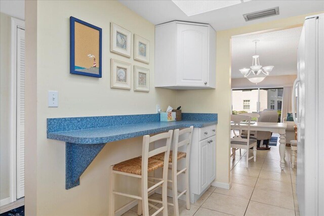 kitchen featuring hanging light fixtures, white cabinets, light tile patterned floors, and a notable chandelier