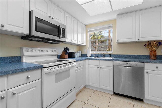 kitchen with appliances with stainless steel finishes, light tile patterned flooring, white cabinetry, and a skylight