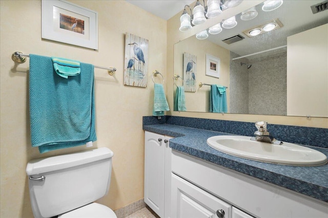 bathroom featuring a tile shower, vanity, and toilet