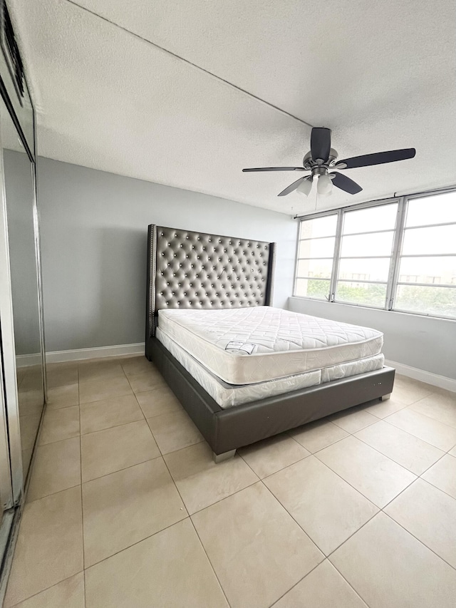 unfurnished bedroom with ceiling fan, a textured ceiling, a closet, and light tile patterned flooring