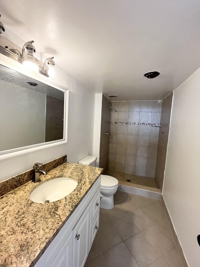 bathroom with a tile shower, tile patterned flooring, vanity, and toilet