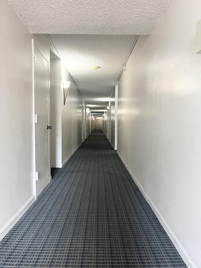 hallway featuring a textured ceiling and dark colored carpet