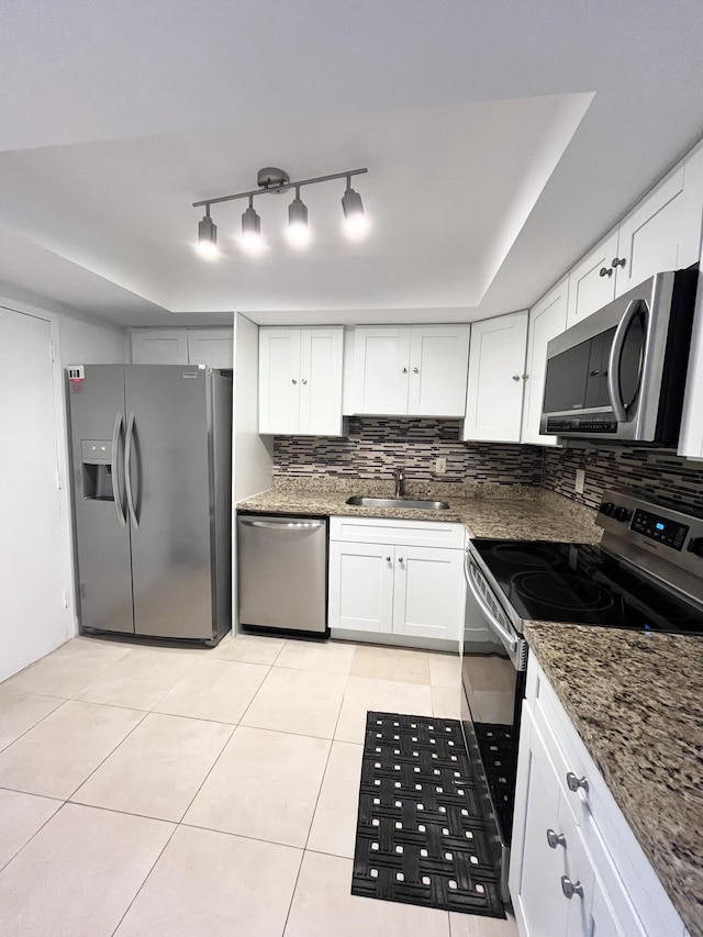 kitchen featuring appliances with stainless steel finishes, white cabinetry, backsplash, dark stone counters, and sink