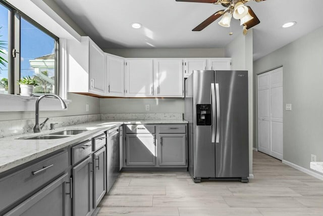 kitchen with light stone countertops, appliances with stainless steel finishes, sink, gray cabinets, and white cabinetry