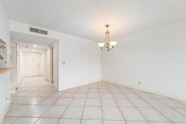 tiled empty room featuring an inviting chandelier and a textured ceiling